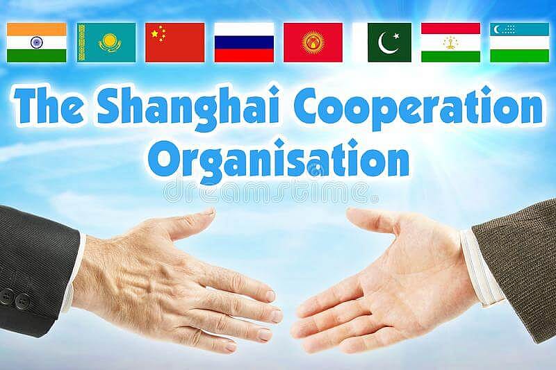 Auf diesem Bild sind alle Flaggen der mitgliedsstatten der Shanghai Cooperation Organisation und 2 Menschen, die sich die Hände reichen 