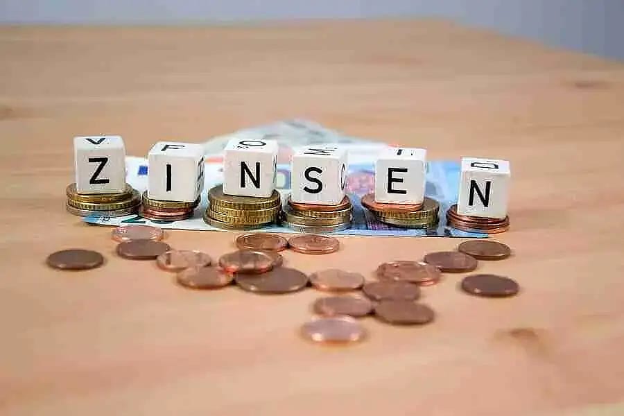 Auf diesem Bild sind Münzen, Scheine und Würfel zu sehen, die Würfel bilden das Wort Zinsen