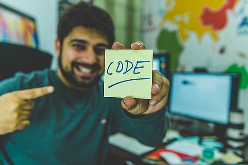 Auf dem Bild sieht man einen Programmierer, der einen Zettel mit dem Wort "Code" hochhält